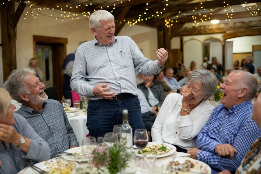 A table of friends in fits of laughter as one mate plays air guitar
